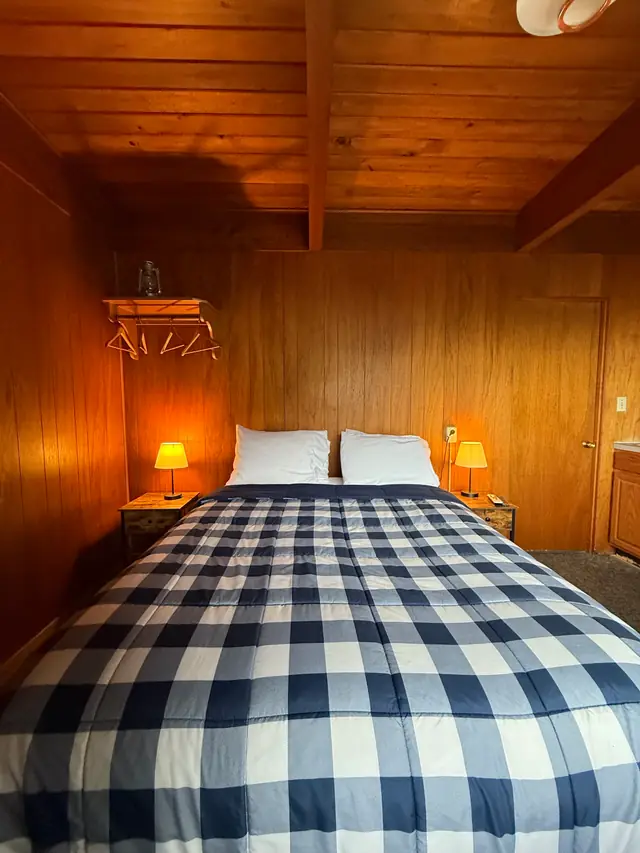 Queen bed with navy buffalo-check bedding in a cedar-panelled room