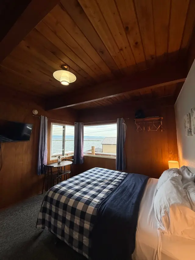 Queen bed with a buffalo-check throw beside a window over the water