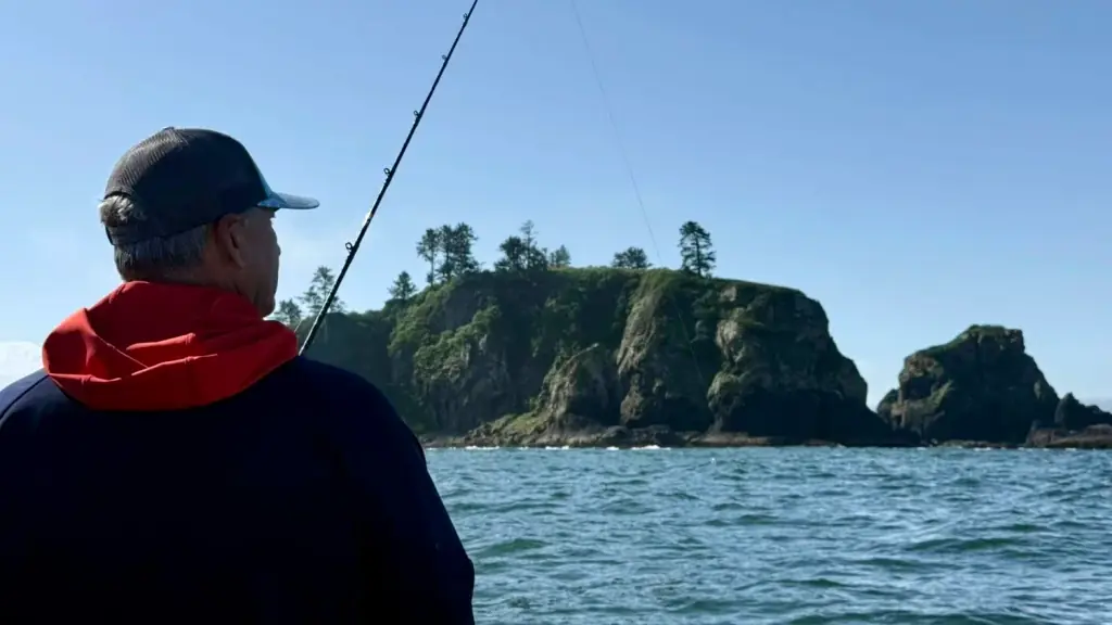 An angler with a rod looking out at a rocky headland on the Strait